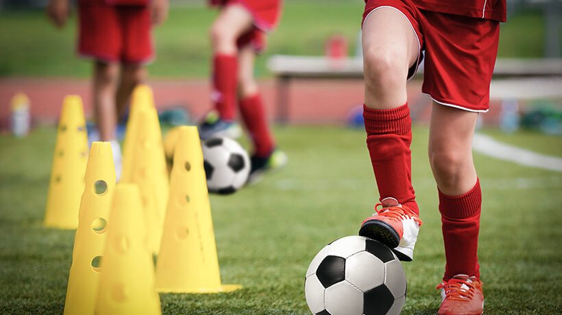 Children kicking soccer balls through cones